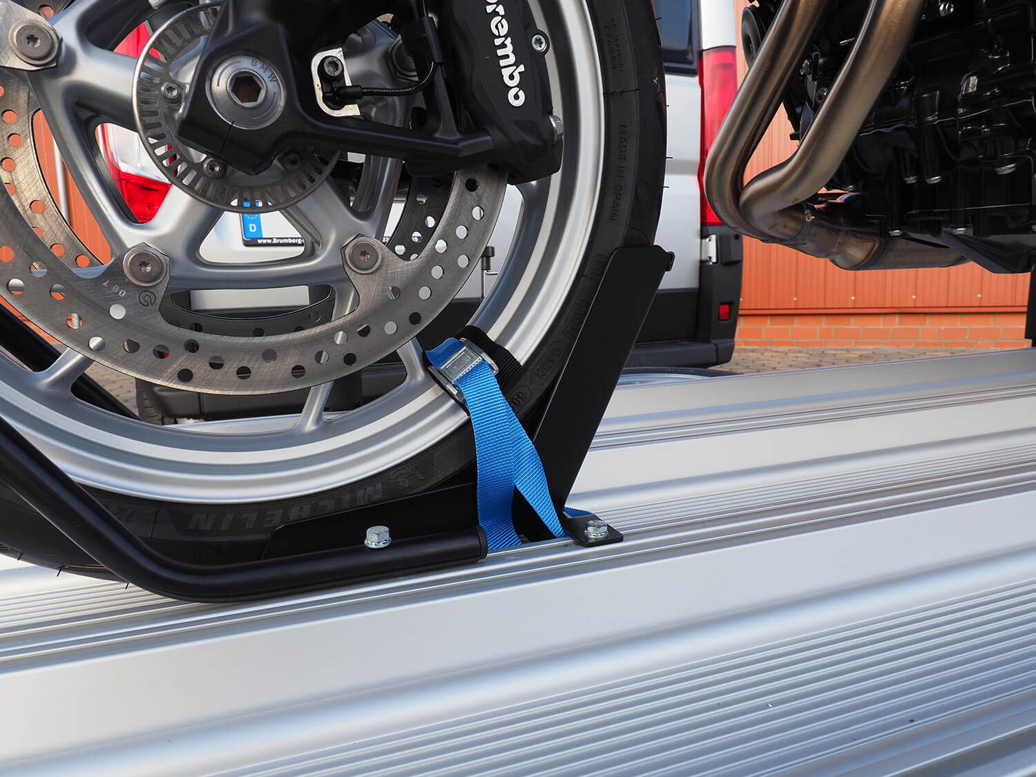 SMV Alu-Star Rolli. Das Vorderrad eines Motorrades mit Spanngurt auf der Plattform gesichert.