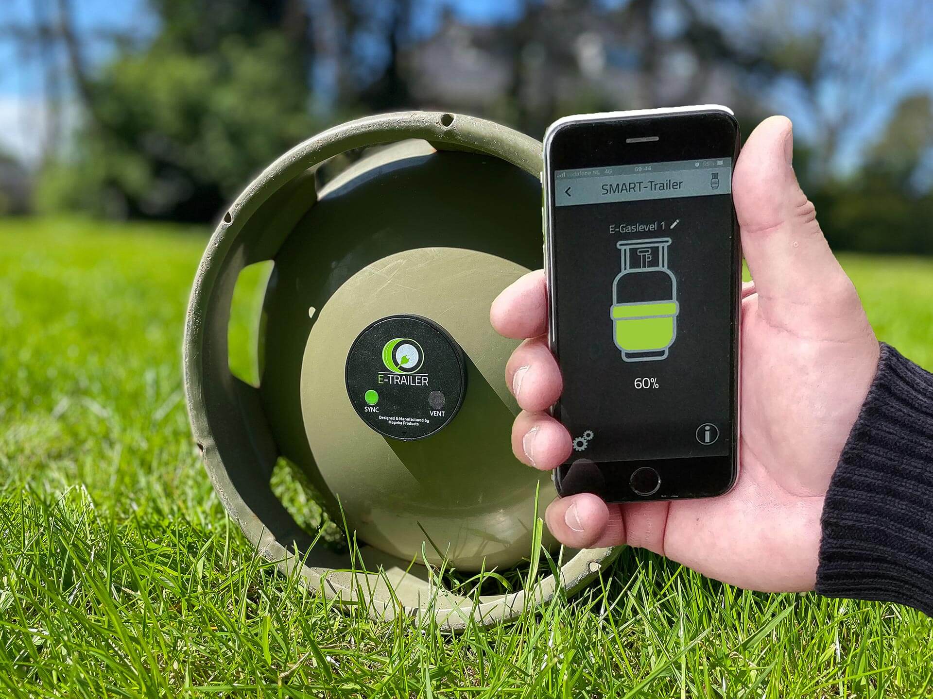 Eine Hand zeigt ein Smartphone mit dem Füllstand der im Hintergrund liegenden Gasflasche.