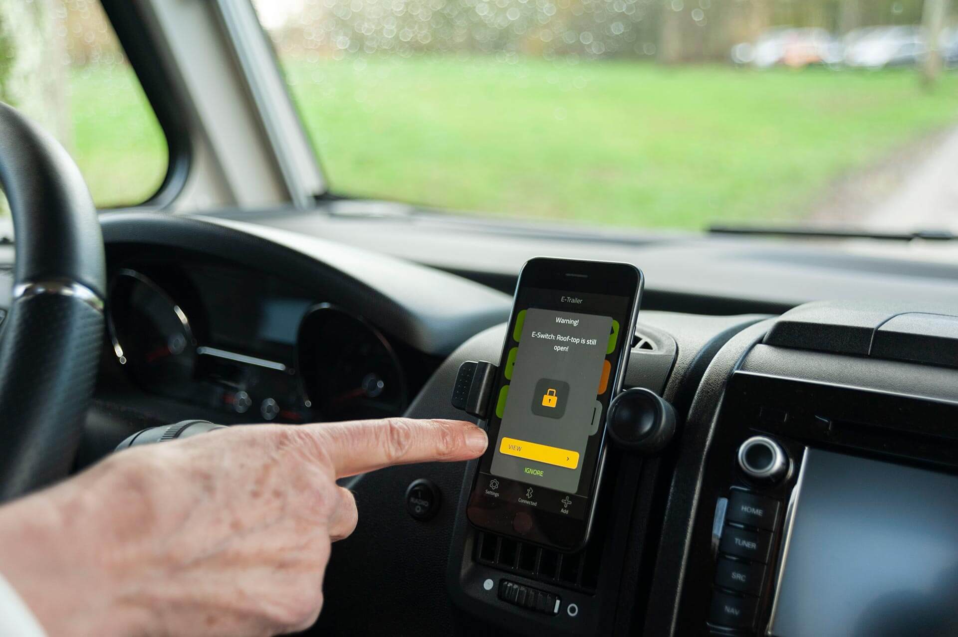 Hand zeigt im Cockpit eines Wohnmobils auf Smartphone mit E-Switch Warnmeldung.
