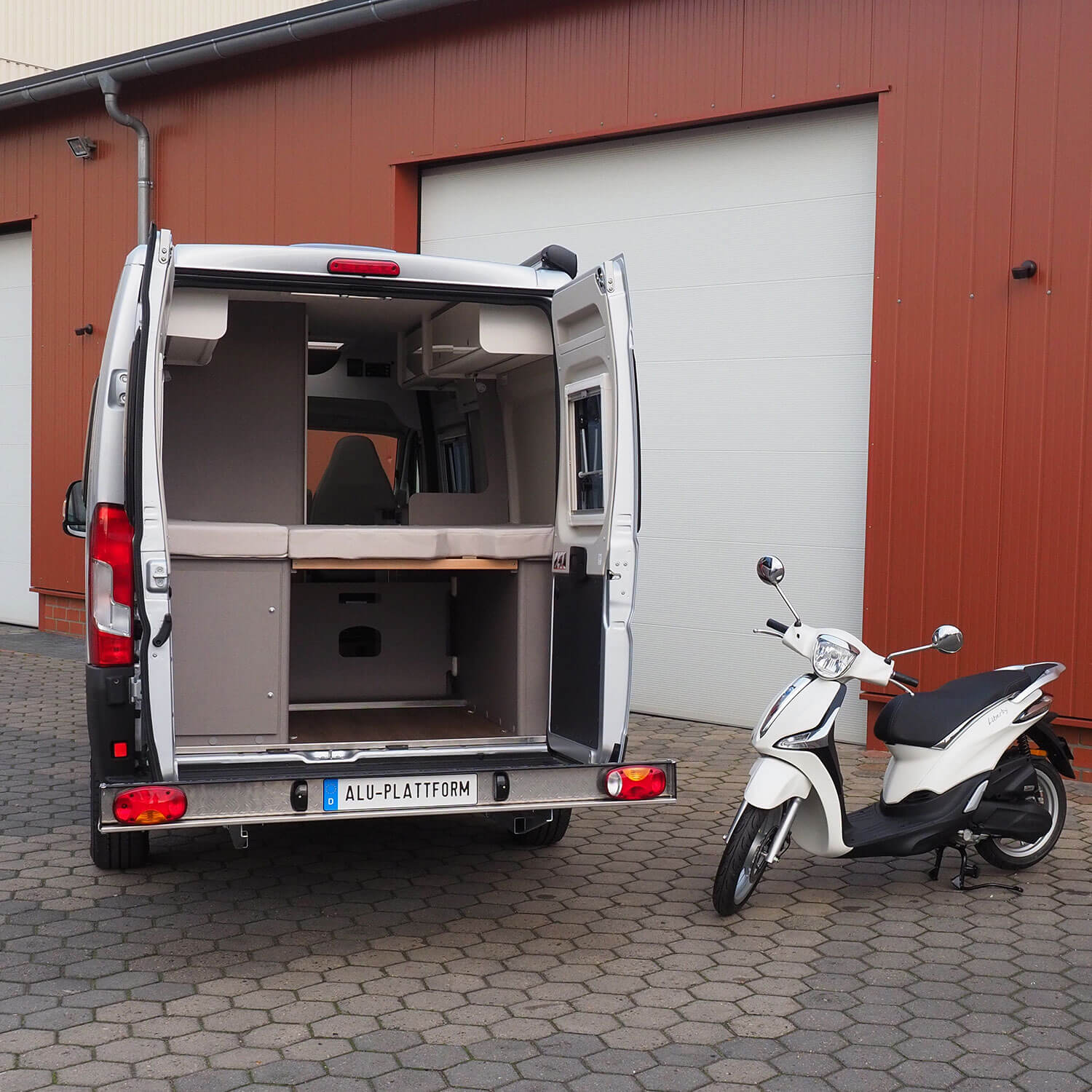 Heckansicht Camper mit montierter Alu Plattform und danebenstehendem Roller.