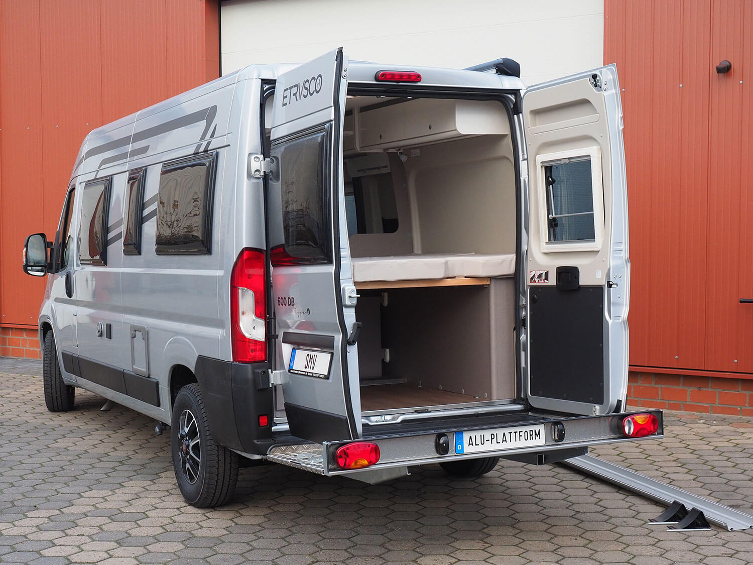 Seitenansicht SMV Alu-Plattform Kastenwagen mit geöffneten Hecktüren. Auffahrrampe und Keile liegen daneben.