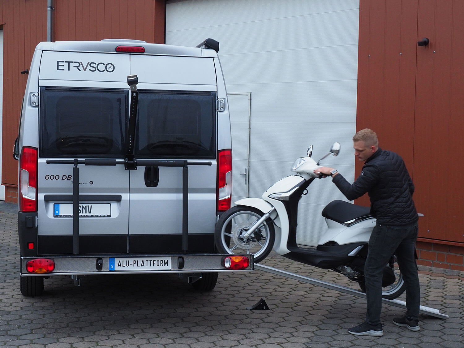 Ein Mann schiebt einen Roller über die Auffahrrampe auf die SMV Alu Plattform.