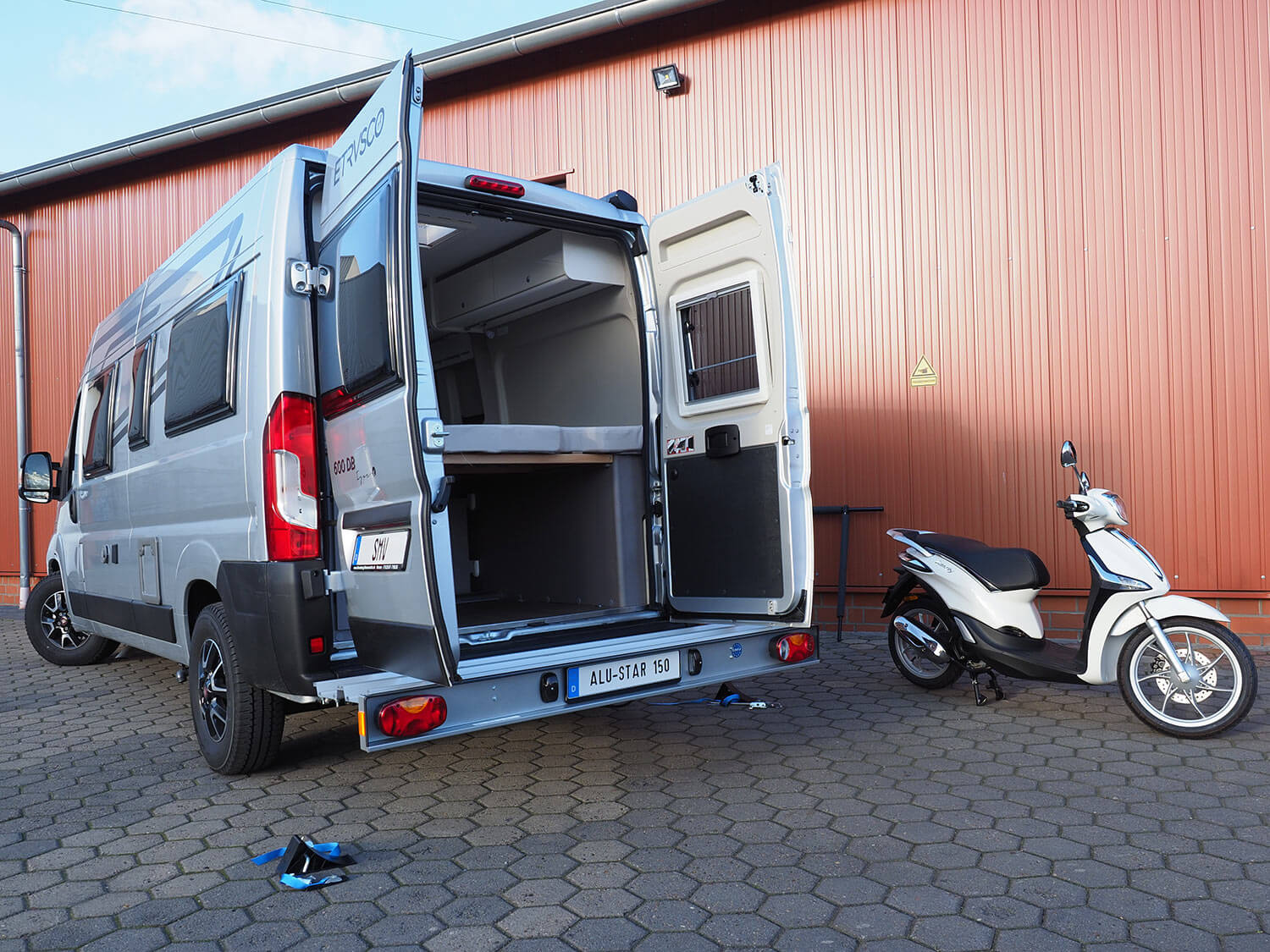 SMV Alu-Star 150 KW montiert an Kastenwagen. Geöffnete Hecktüren und daneben steht ein Roller. 